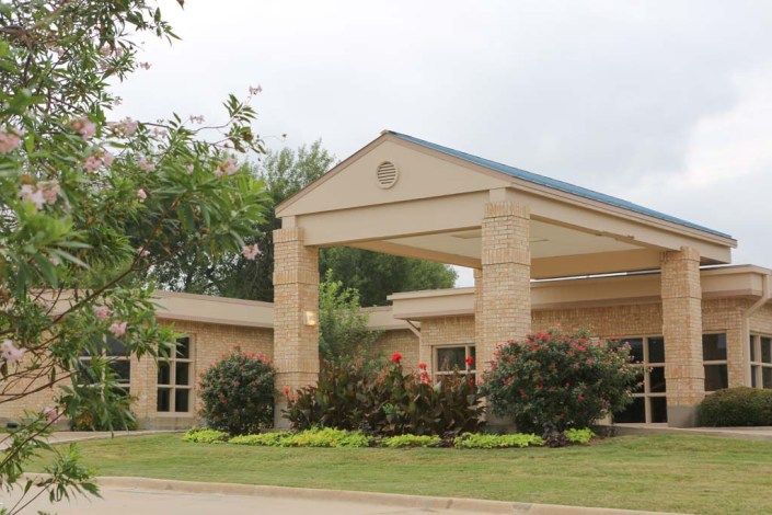 A building entrance with landscaped greenery and a clear sky backdrop.