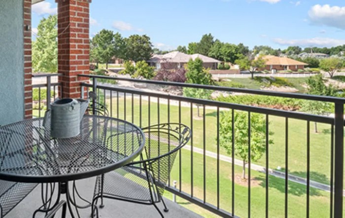 A scenic view from a balcony with a table and chairs overlooking a grassy area and houses.
