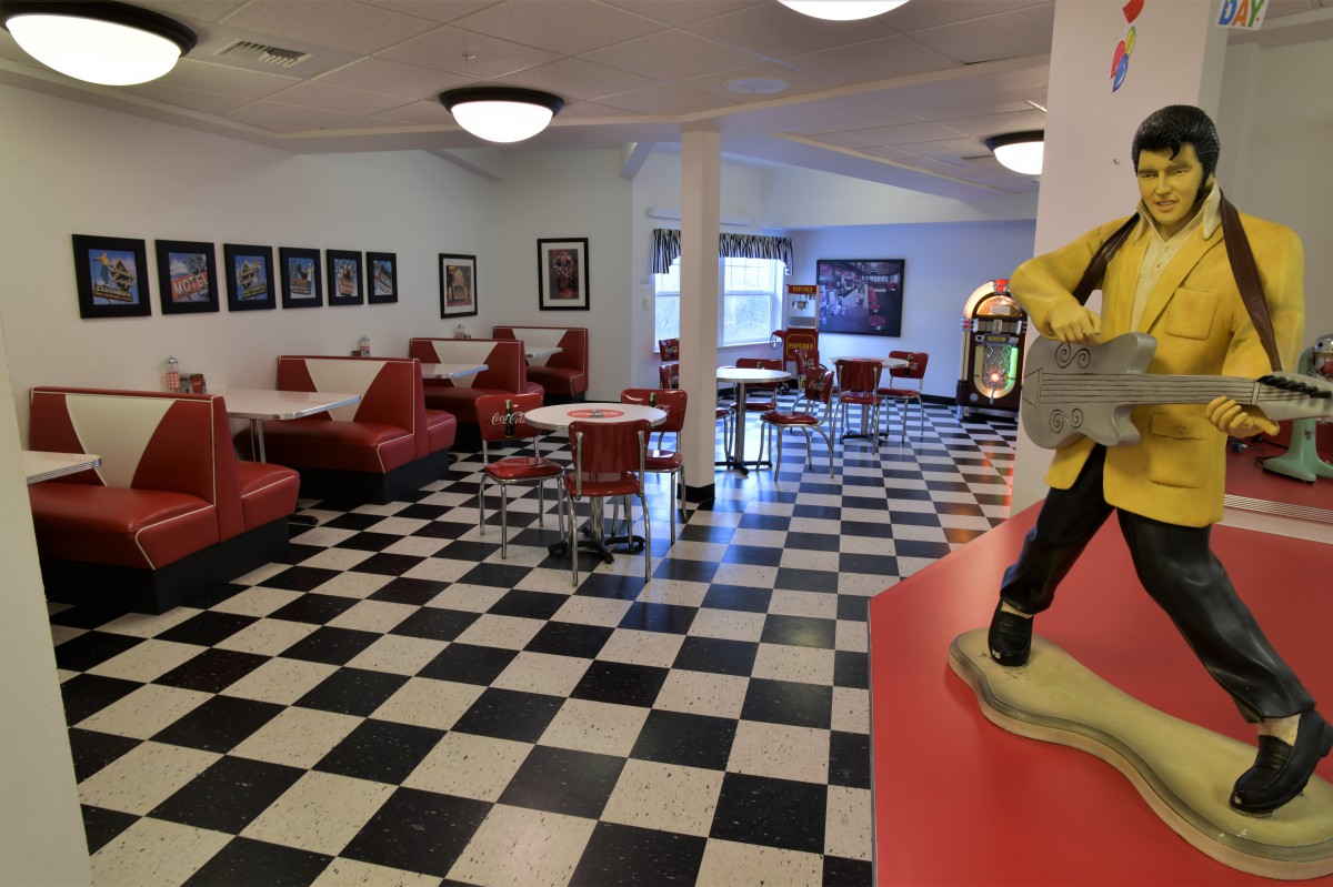 A retro-style diner interior with red booths, a checkered floor, and a jukebox.