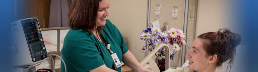 A smiling nurse providing care in a hospital environment with flowers in the background.