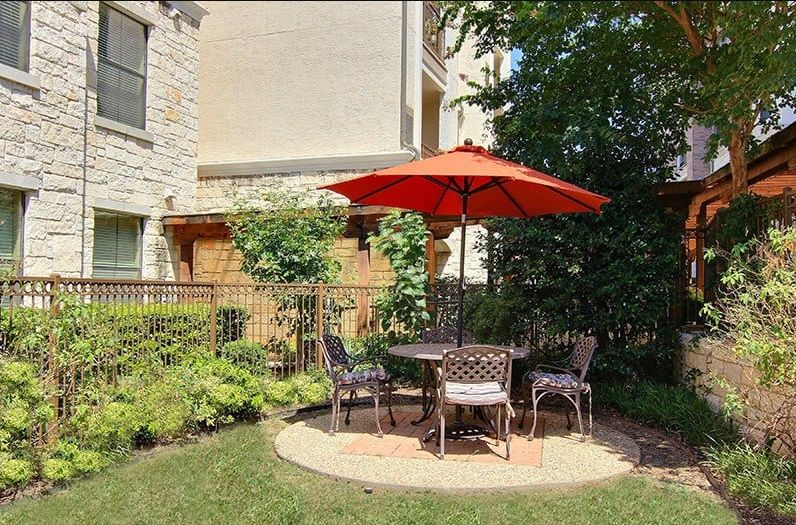 Outdoor patio set with a red umbrella and chairs in a garden setting.