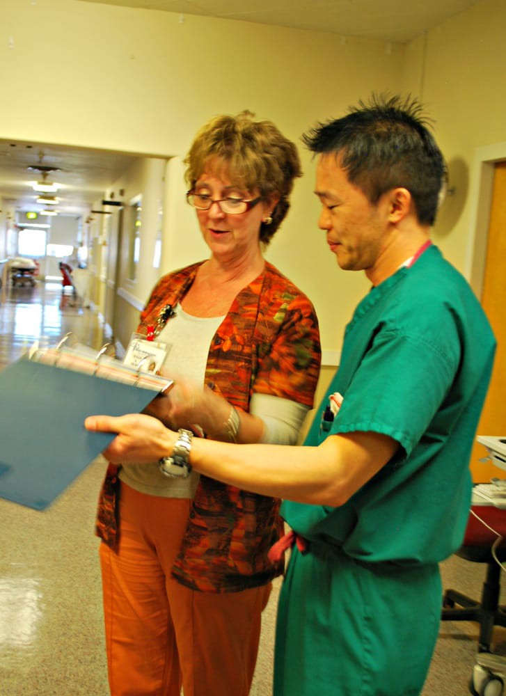 Two healthcare professionals discussing a patient's chart in a hospital corridor.
