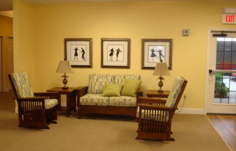 A cozy living room with a sofa, chairs, and artwork on a yellow wall.