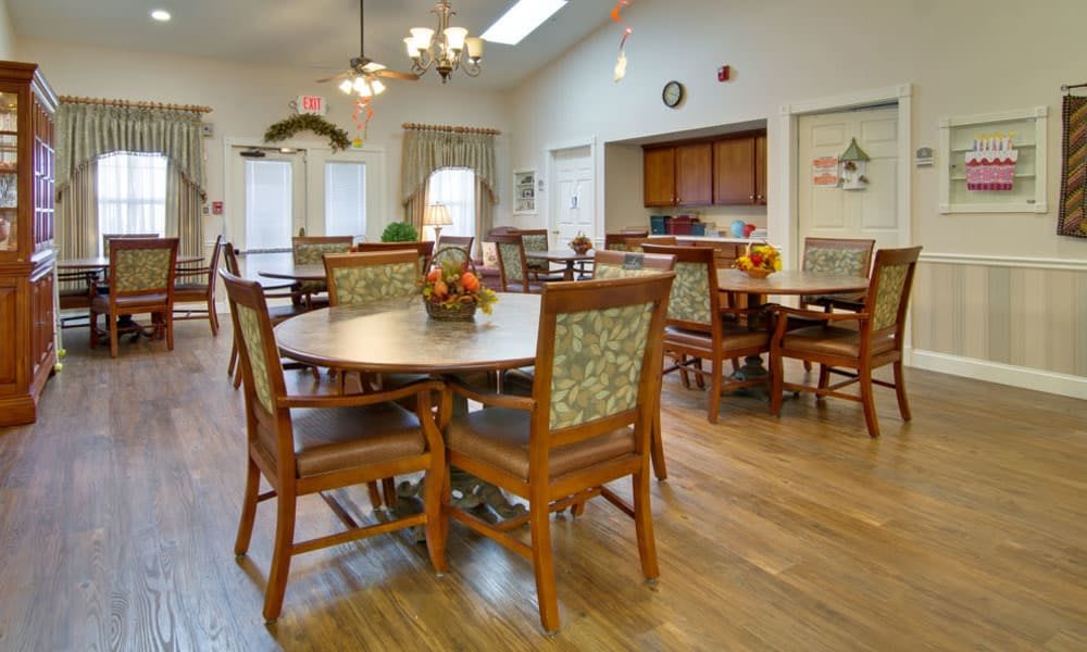 A spacious dining area with round tables and comfortable chairs, featuring wooden floors and elegant lighting fixtures.