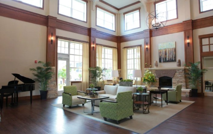 A spacious and modern living room with high ceilings and large windows, featuring comfortable green chairs and stylish decor.