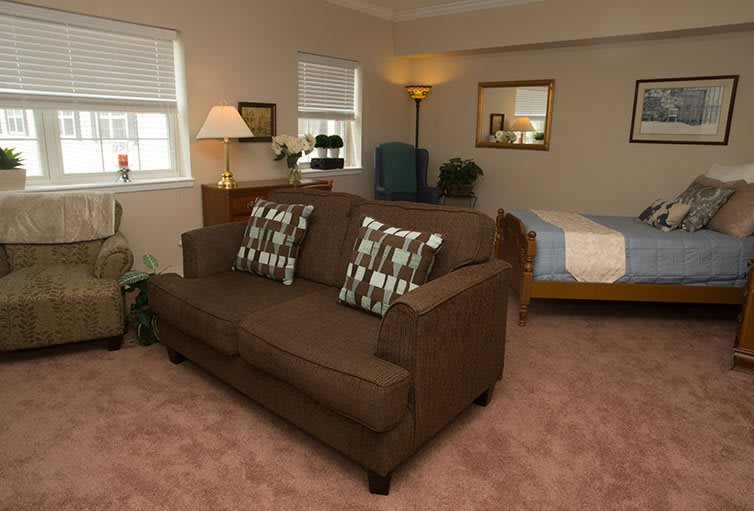 A cozy living area with a brown sofa, pillows, and a bed in the corner.