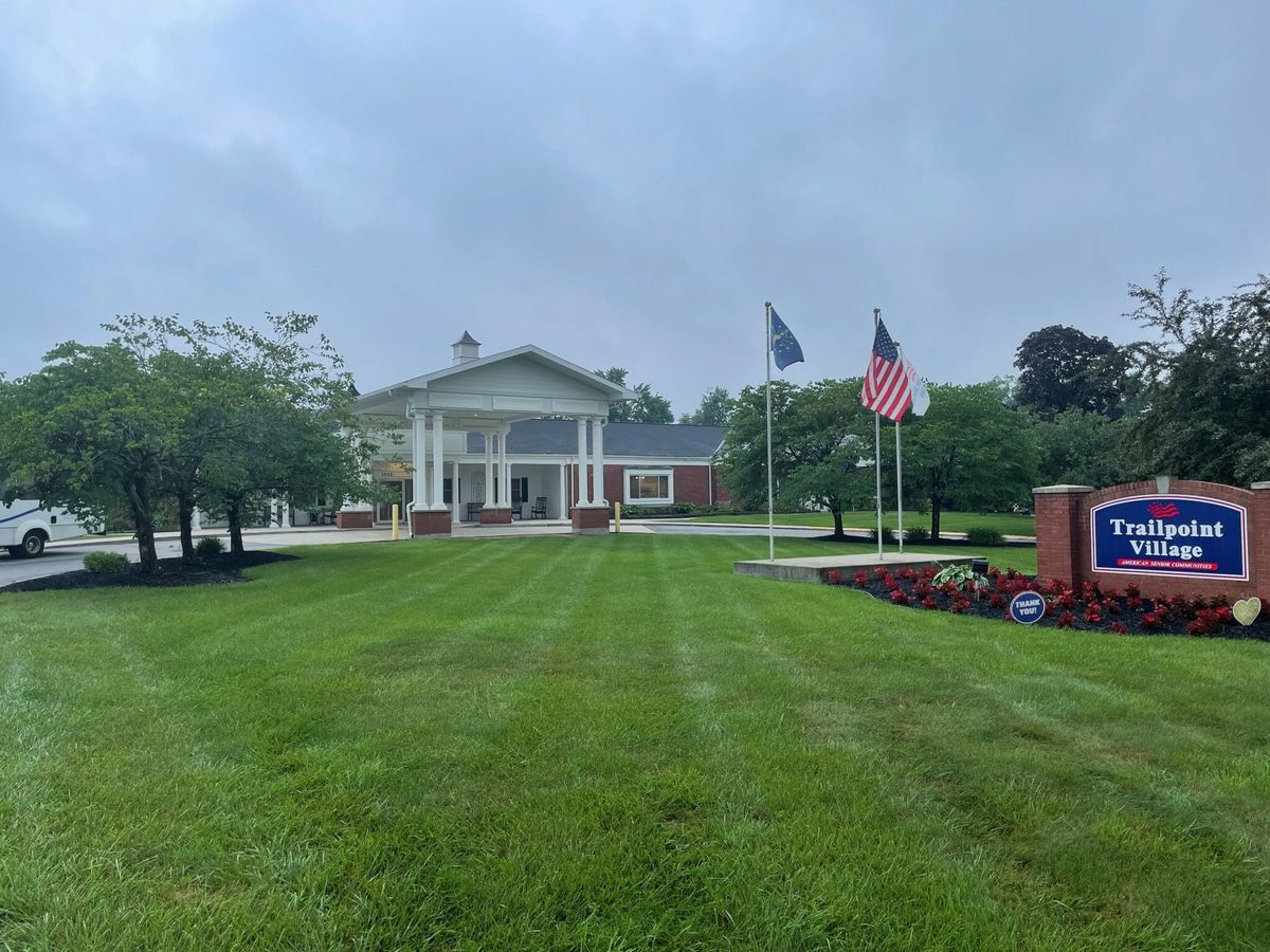 A building surrounded by lush greenery with flags and a sign in the foreground on a cloudy day.