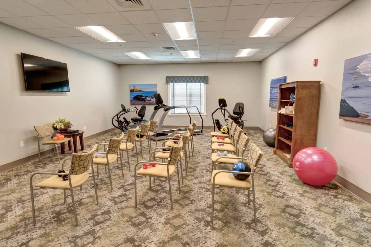 A fitness room with exercise machines, chairs arranged in rows, and gym balls for group activities or classes.