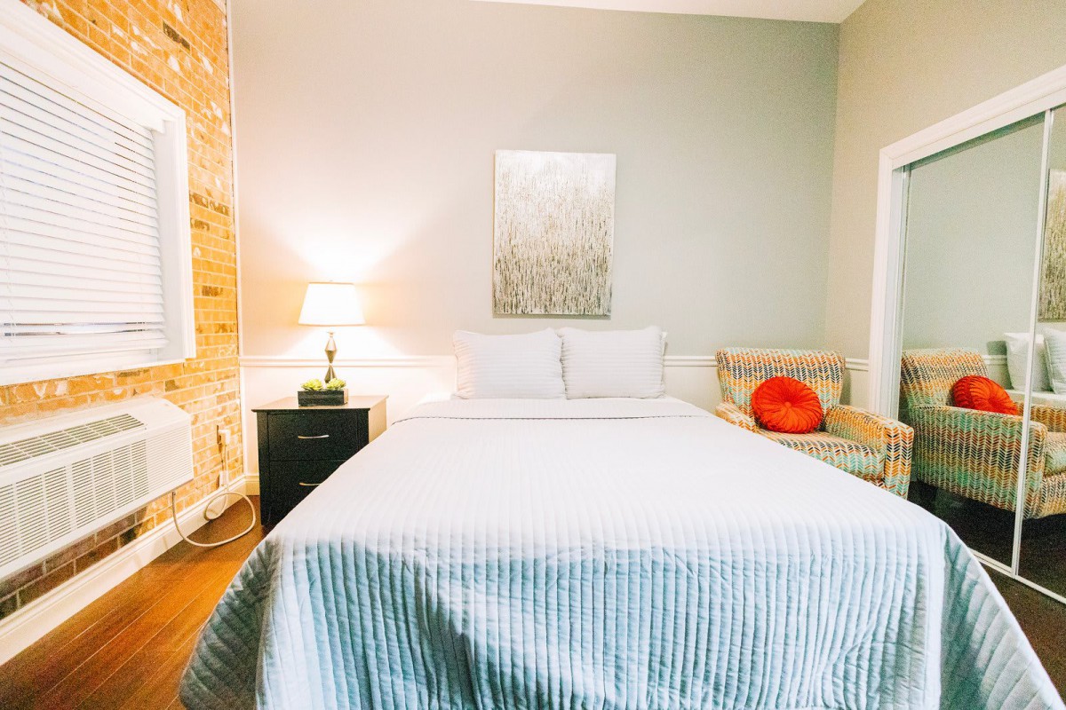 A cozy bedroom with a neatly made bed, side table lamp, and wall artwork.