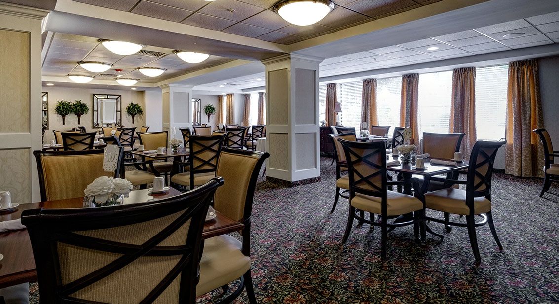A spacious indoor restaurant dining area with elegantly arranged tables and chairs, featuring large windows and soft lighting.