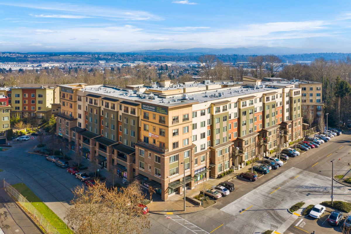 Aerial view of a multi-story apartment building with a parking lot in an urban setting.