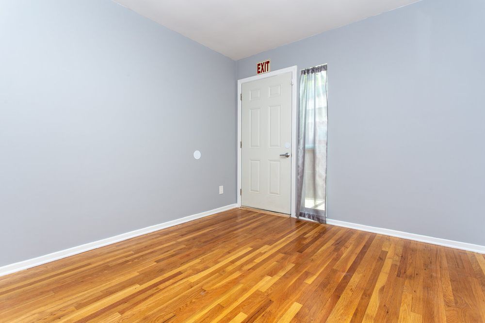 An empty room with a hardwood floor and a white door adorned with curtains.