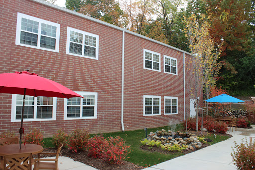 A brick building featuring multiple windows, set in a landscaped area with outdoor seating.