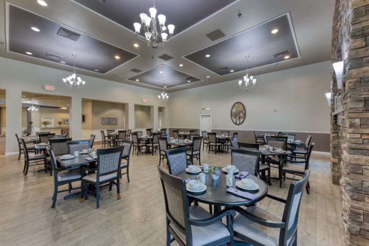 An elegant dining room with neatly arranged tables and chairs, illuminated by chandeliers.