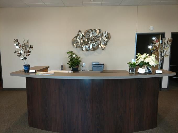 A modern office reception desk with decorative plants and artwork on the wall.