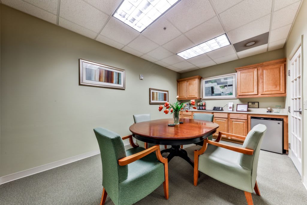 A small meeting room with a round wooden table and four chairs, decorated with paintings on the walls.