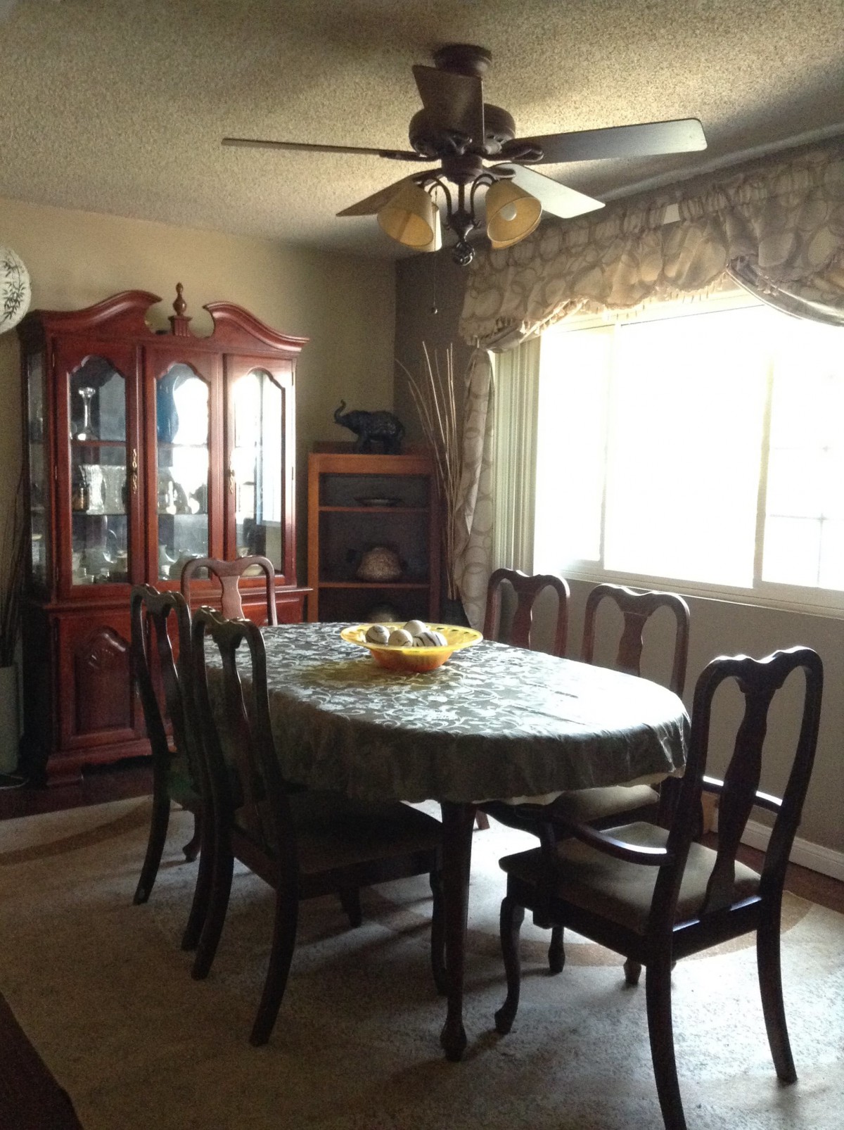 A cozy dining room with a wooden table and chairs, a display cabinet, and a ceiling fan.