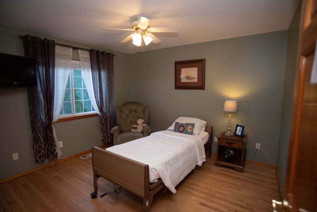 A cozy bedroom with a single bed, lamp, and armchair next to a window with curtains.