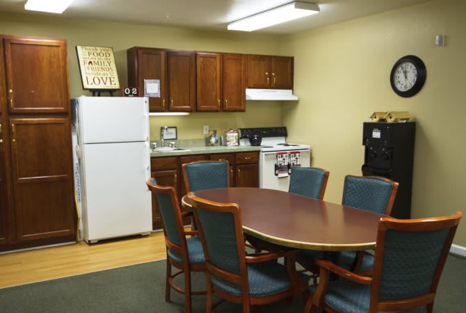 Office kitchen with a round table and chairs, equipped with a refrigerator and stove.