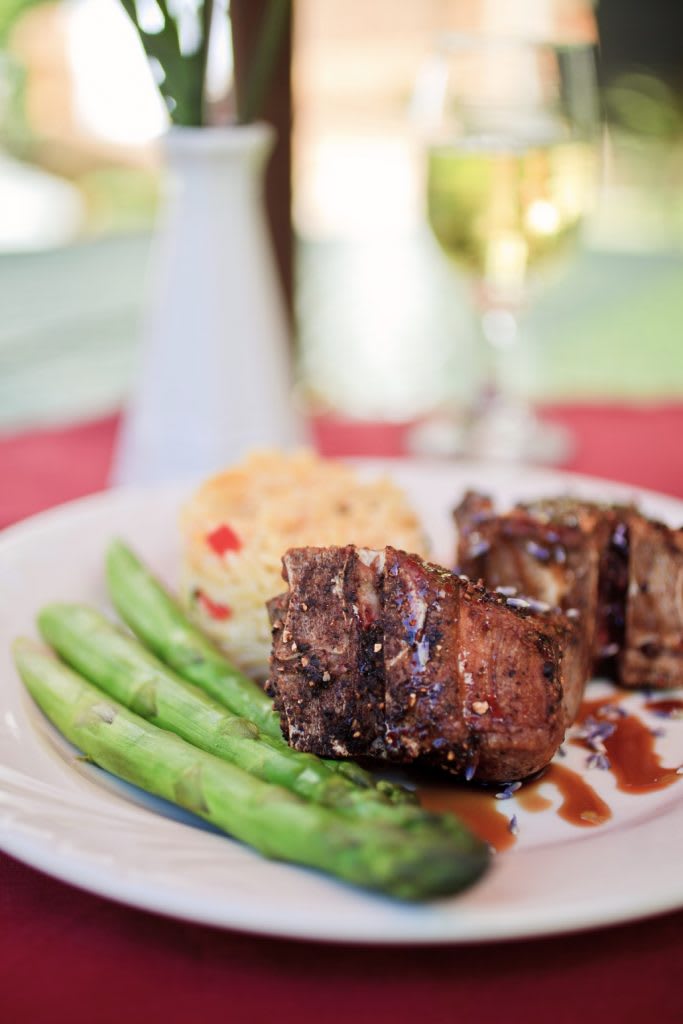 A gourmet dinner featuring steak, asparagus, and a side dish, served with wine.