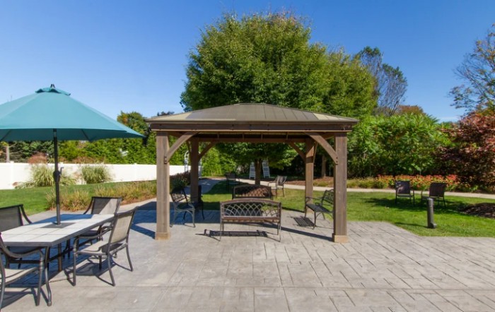 A sunny day in a backyard with a gazebo and patio furniture, including a swing.