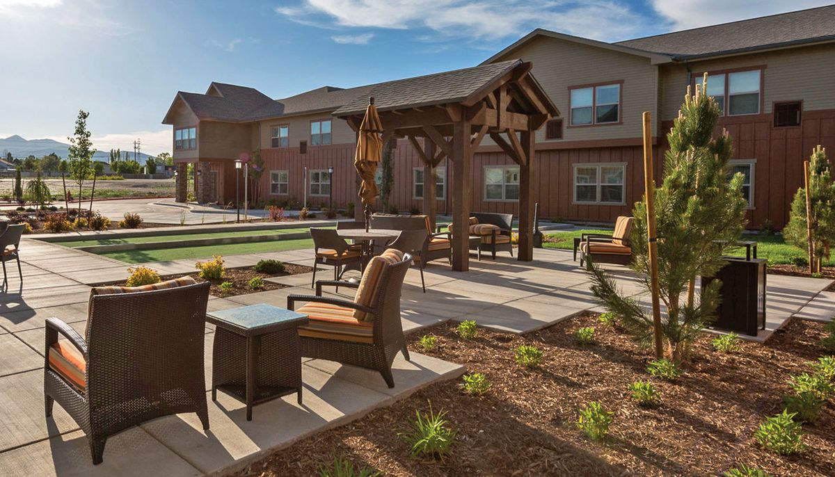 A well-maintained outdoor patio area with comfortable seating and a landscaped garden, set against the backdrop of a modern building on a sunny day.