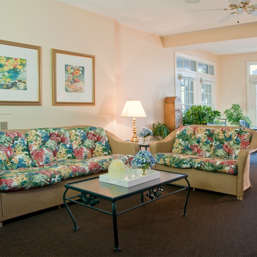 A cozy living room featuring floral-patterned sofas, a glass-topped coffee table, and decorative artwork on the walls.