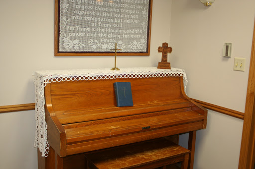 A wooden piano placed in a church setting, accompanied by a decorative cross and religious text.