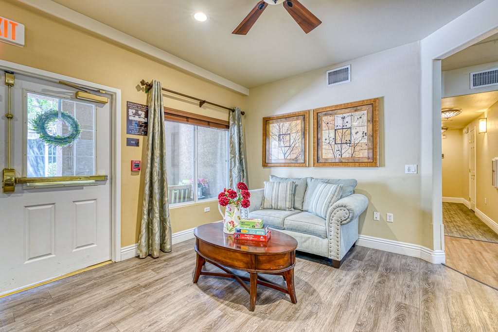 A cozy living room with a sofa, wooden coffee table, and large windows, featuring a ceiling fan and warm lighting.