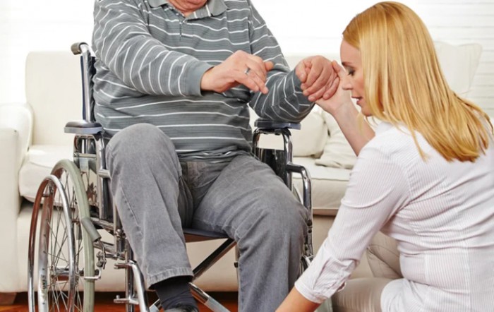 A caregiver assists an elderly man in a wheelchair indoors.