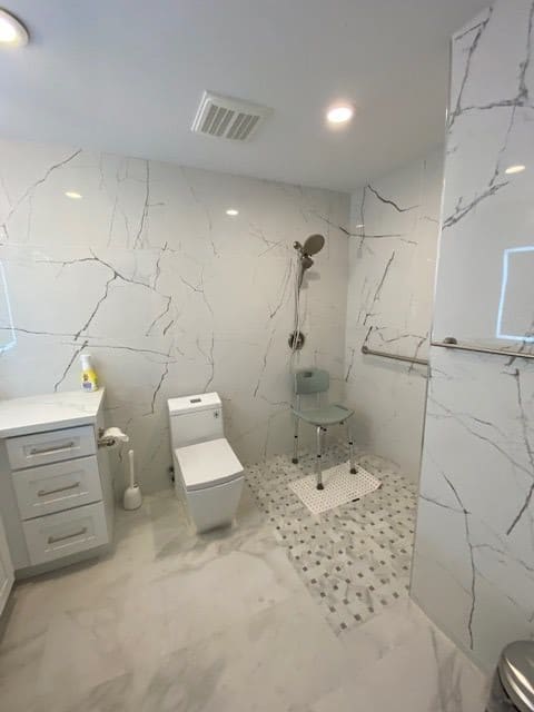 A modern bathroom with marble tiles, featuring a toilet, sink, and walk-in shower.