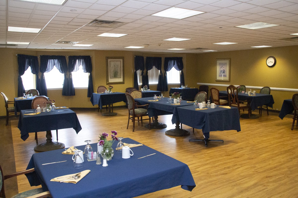 A spacious dining room with tables covered in blue tablecloths, set for a meal.
