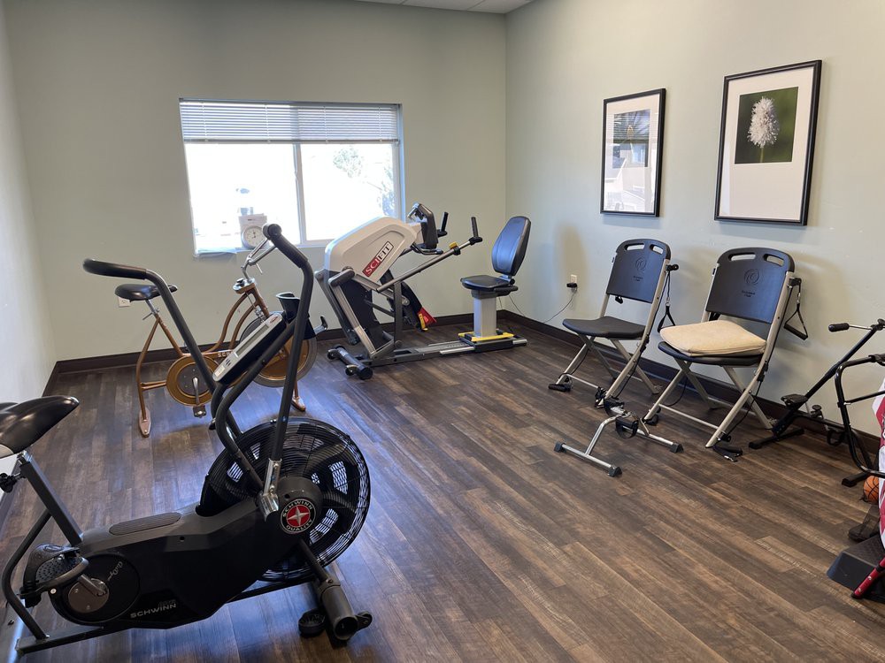 A small gym with exercise bikes and chairs on a wooden floor.
