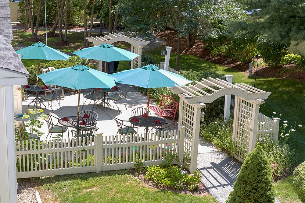 A beautifully designed outdoor patio area featuring tables with blue umbrellas, surrounded by lush greenery and a white lattice fence.