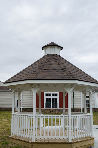 A charming wooden gazebo with a conical roof, set against a backdrop of cloudy skies.