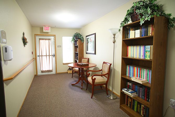 A cozy hallway with a table and chairs, a bookshelf full of books, a standing lamp, and decorative plants.