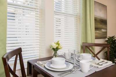 A neatly set dining table with white dinnerware, glasses, and a small vase of flowers by the window.