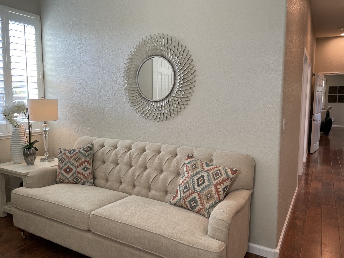 A stylish living room featuring a beige tufted sofa with patterned cushions, a decorative round mirror on the wall, and a lamp providing cozy lighting.