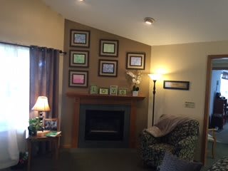 A cozy living room featuring a fireplace, framed pictures on the wall, and warm lighting from lamps.