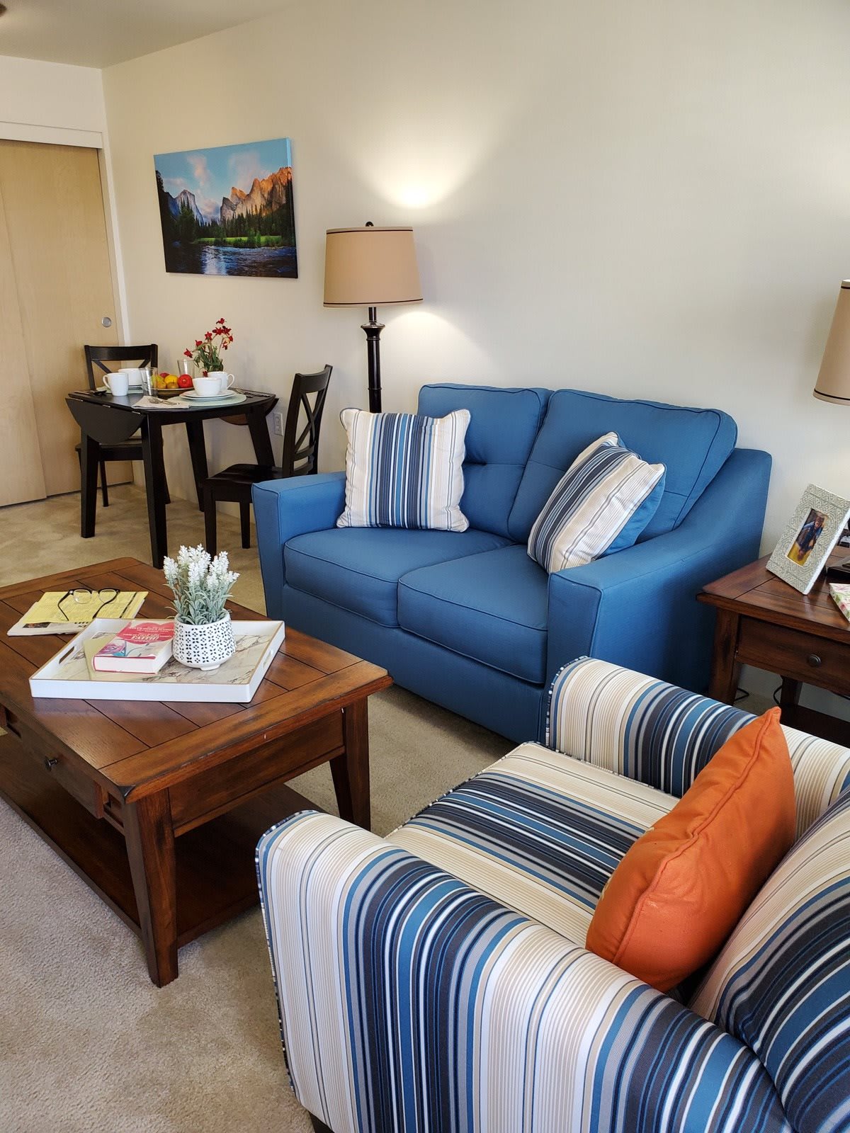 A cozy living room with a blue sofa, striped armchair, and wooden coffee table adorned with decorative items.