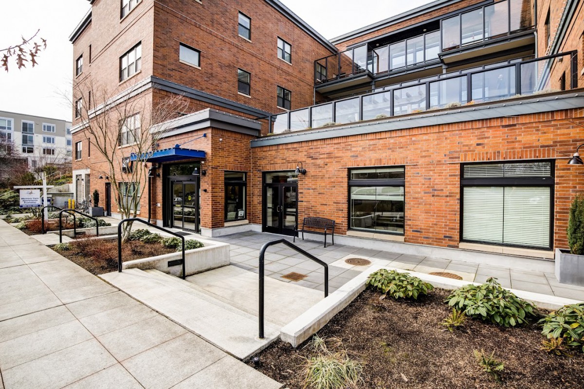 A modern brick building with glass windows and a landscaped entrance.