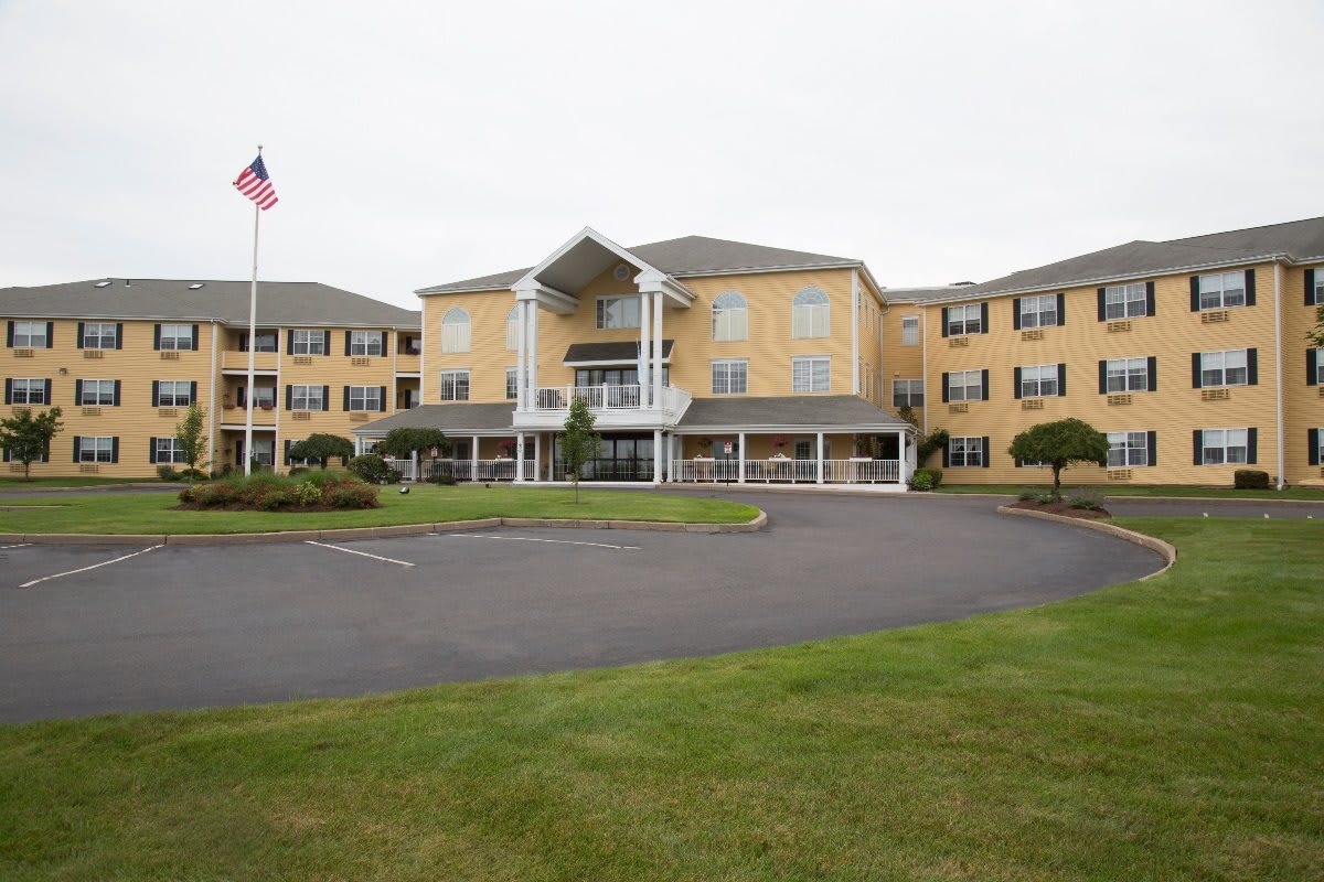 A large, multi-story building with a flagpole in front and a landscaped parking area.