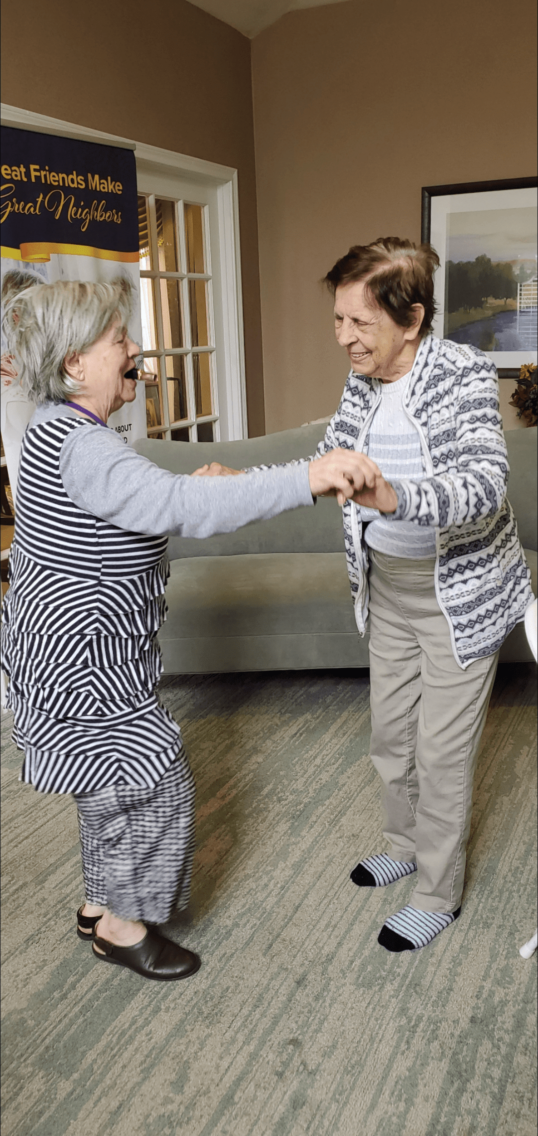 Two elderly women joyfully dancing together indoors.