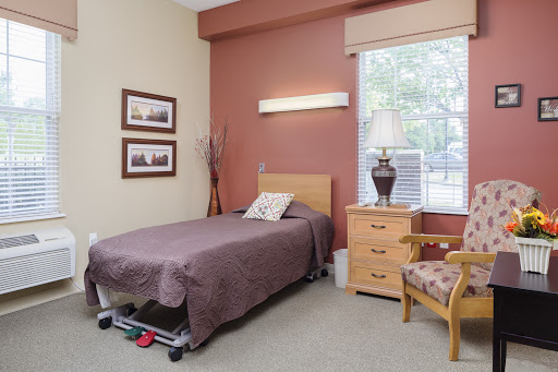A cozy bedroom featuring a single bed, nightstand with a lamp, and warm-toned walls.