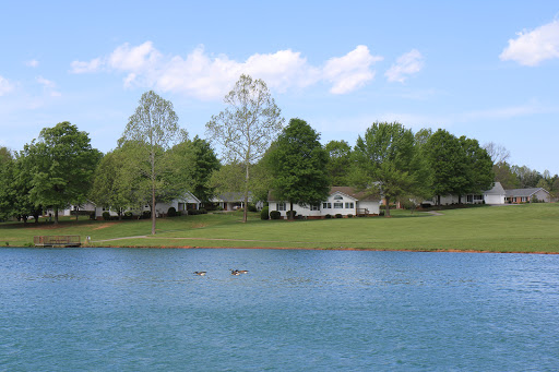 A serene view of a lake surrounded by lush greenery and homes under a clear blue sky.