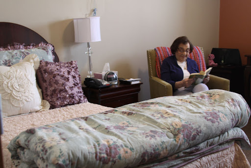 A cozy bedroom scene featuring a person reading in an armchair next to a neatly made bed.