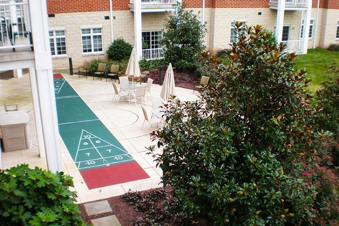 A courtyard featuring a shuffleboard court surrounded by greenery and seating areas.
