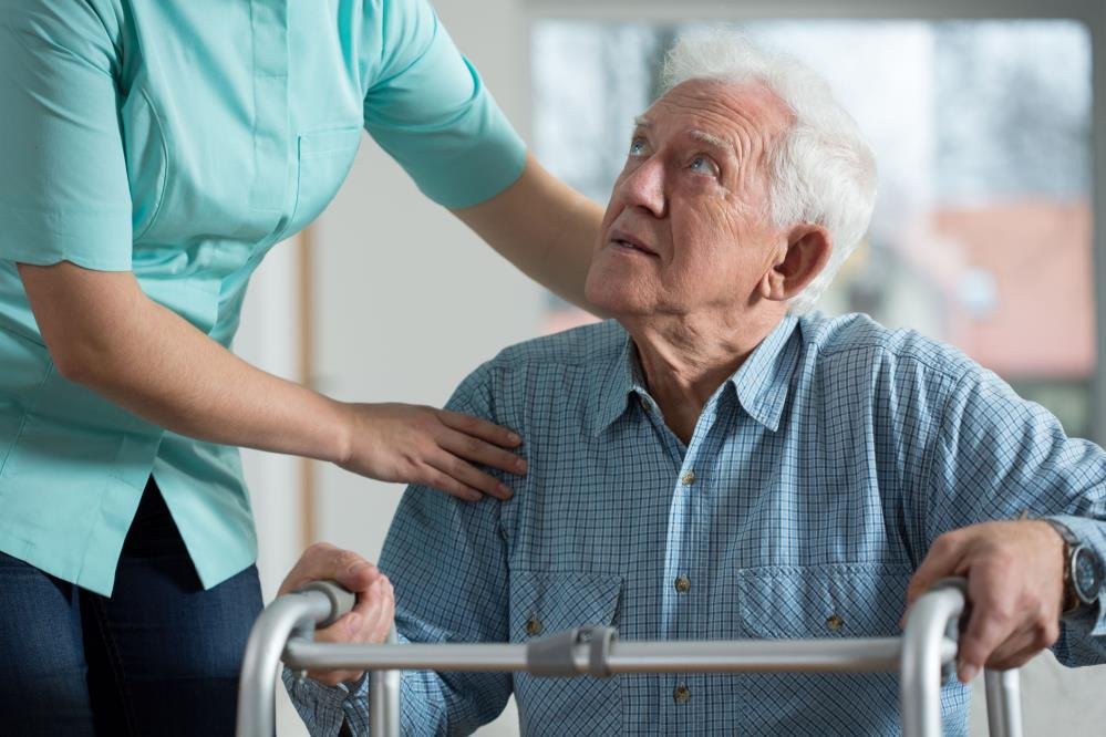A caregiver assisting an elderly man using a walker.