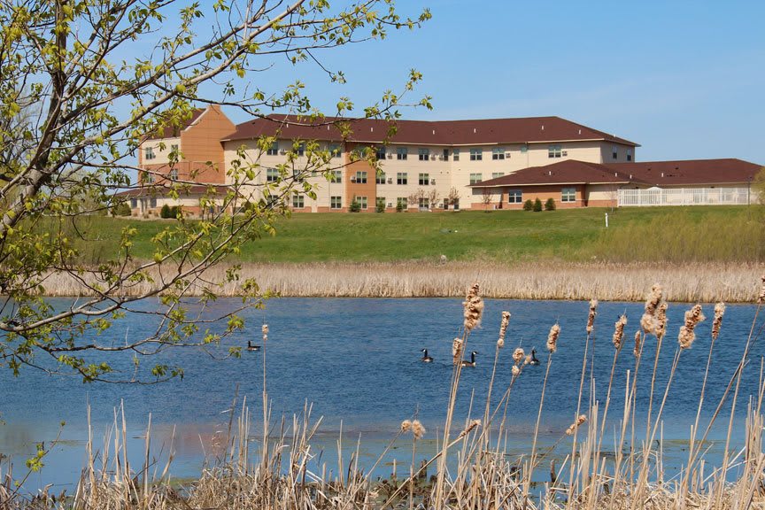 A building by a lake with surrounding nature and clear skies.