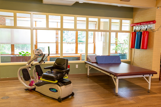 A bright and inviting therapy room equipped with exercise machines and a treatment table.